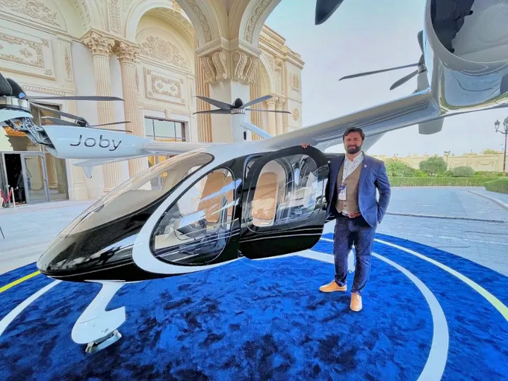 Dan Sloat standing beside a Joby electric air taxi displayed on a blue carpet