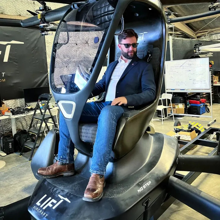 Dan Sloat in sunglasses seated in the cockpit of a single-seat LIFT eVTOL aircraft in a workshop