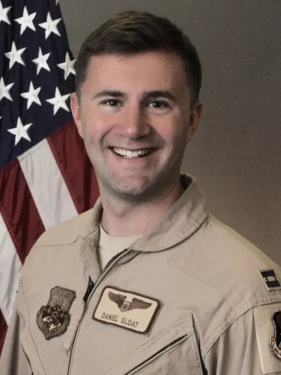 Official US Air Force portrait of Captain Daniel Sloat in a tan flight suit in front of the American flag