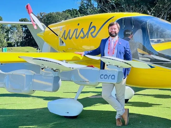 Dan Sloat in a blue blazer leaning on the wing of a yellow Wisk Cora air taxi on a lawn